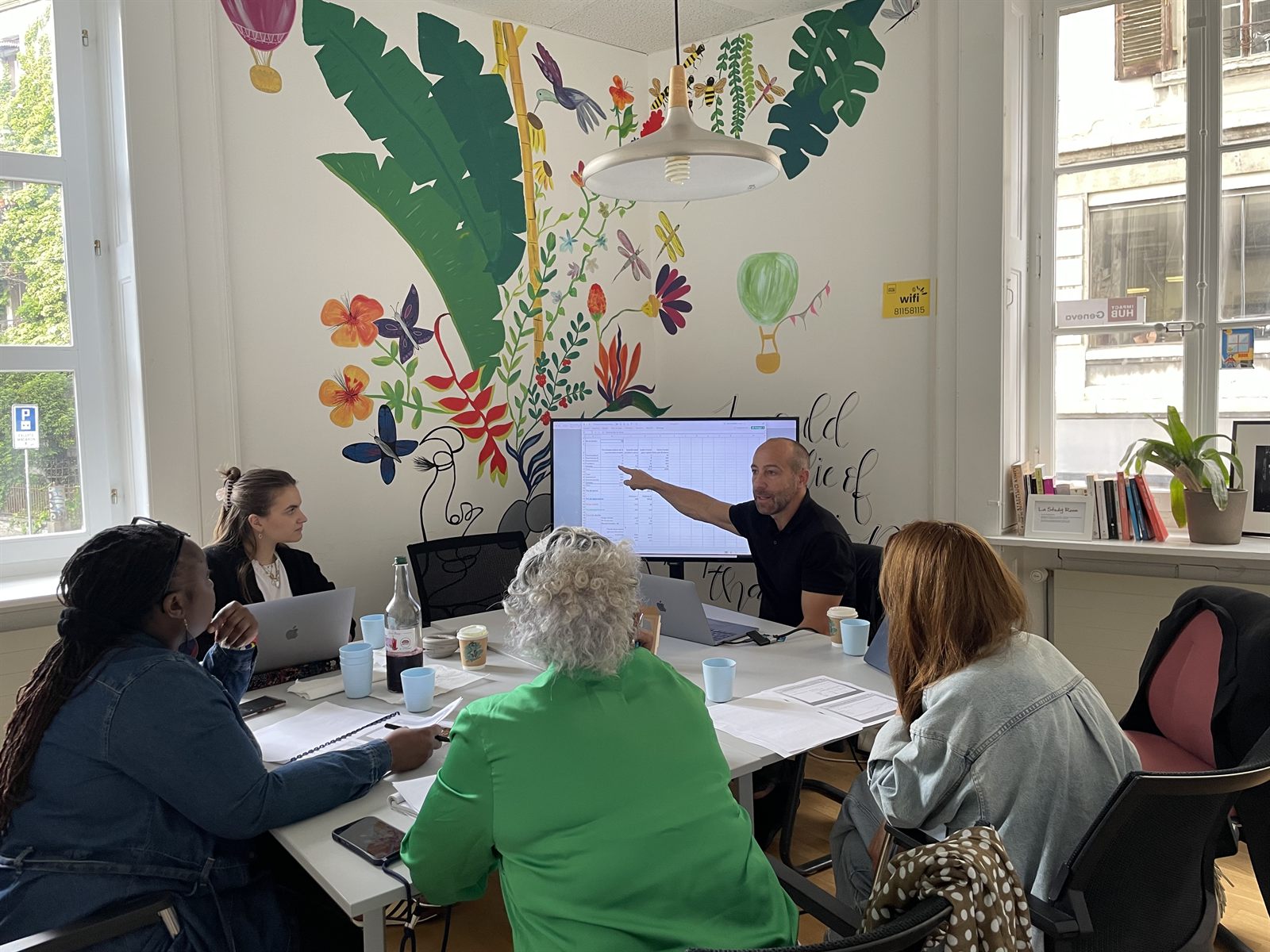 Un mentor bénévole Alter Start partage son expertise autour d'un tableur avec des participants, à l'Impact Hub Genève